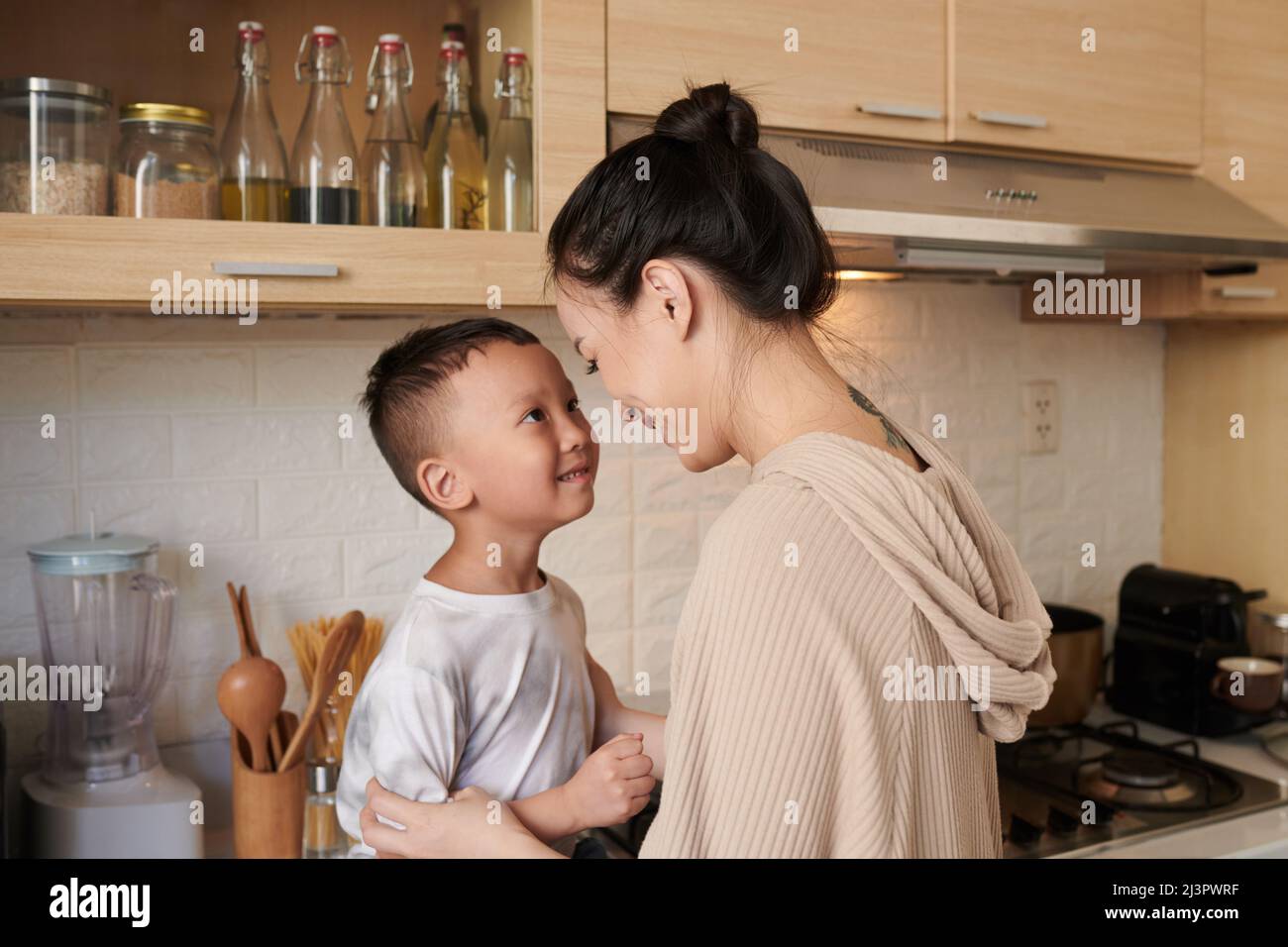 Happy young mother talking to little son sitting on kitchen counter