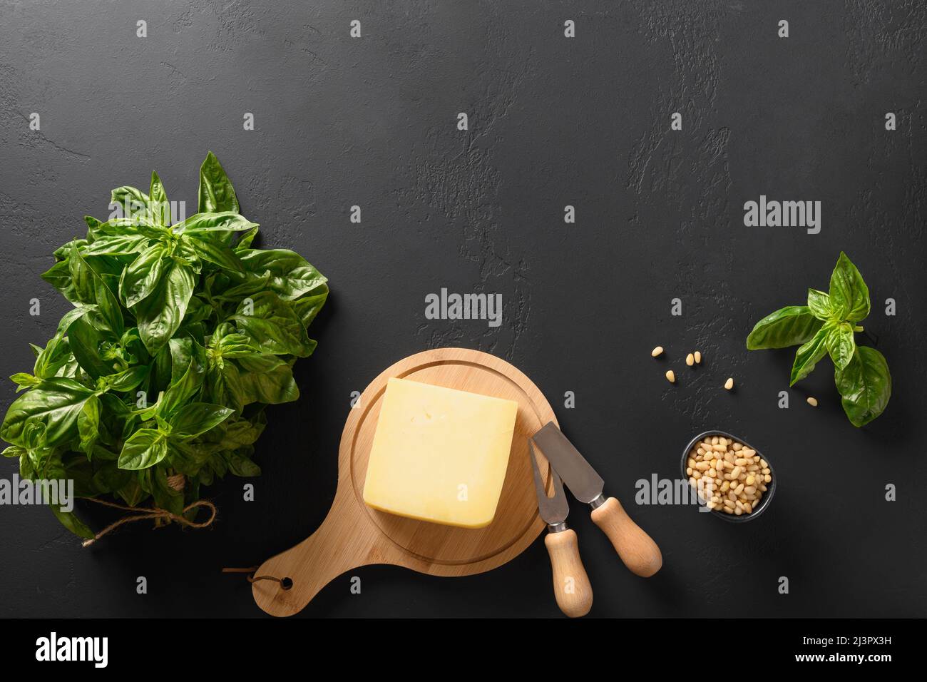 Fresh basil, cedar nuts, olive oil and parmesan cheese and ingredients for homemade pesto on black background with copy space. View from above. Stock Photo