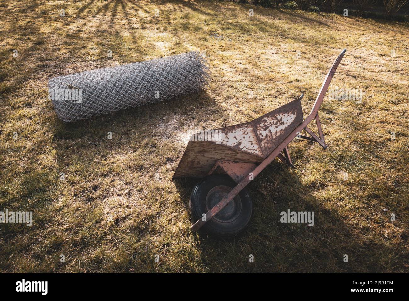 a wheelbarrow lies next to a roll of wire mesh fence Stock Photo - Alamy