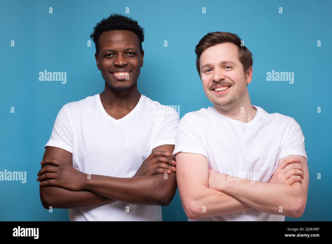 Two young men in casual clothes posing with folded arms and smiling to ...