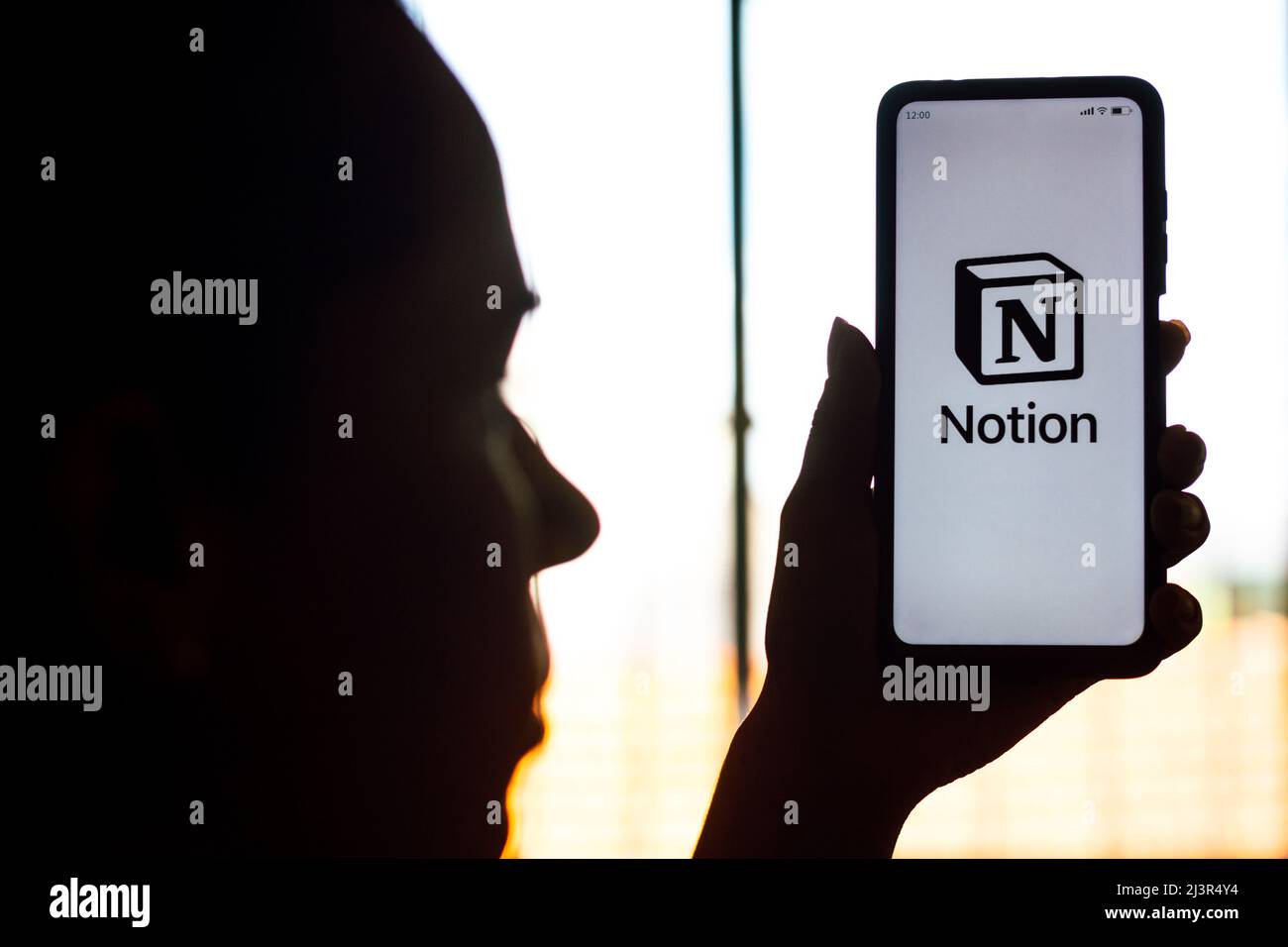 In this photo illustration, a woman's silhouette holds a smartphone with the Notion logo displayed on the screen. Stock Photo