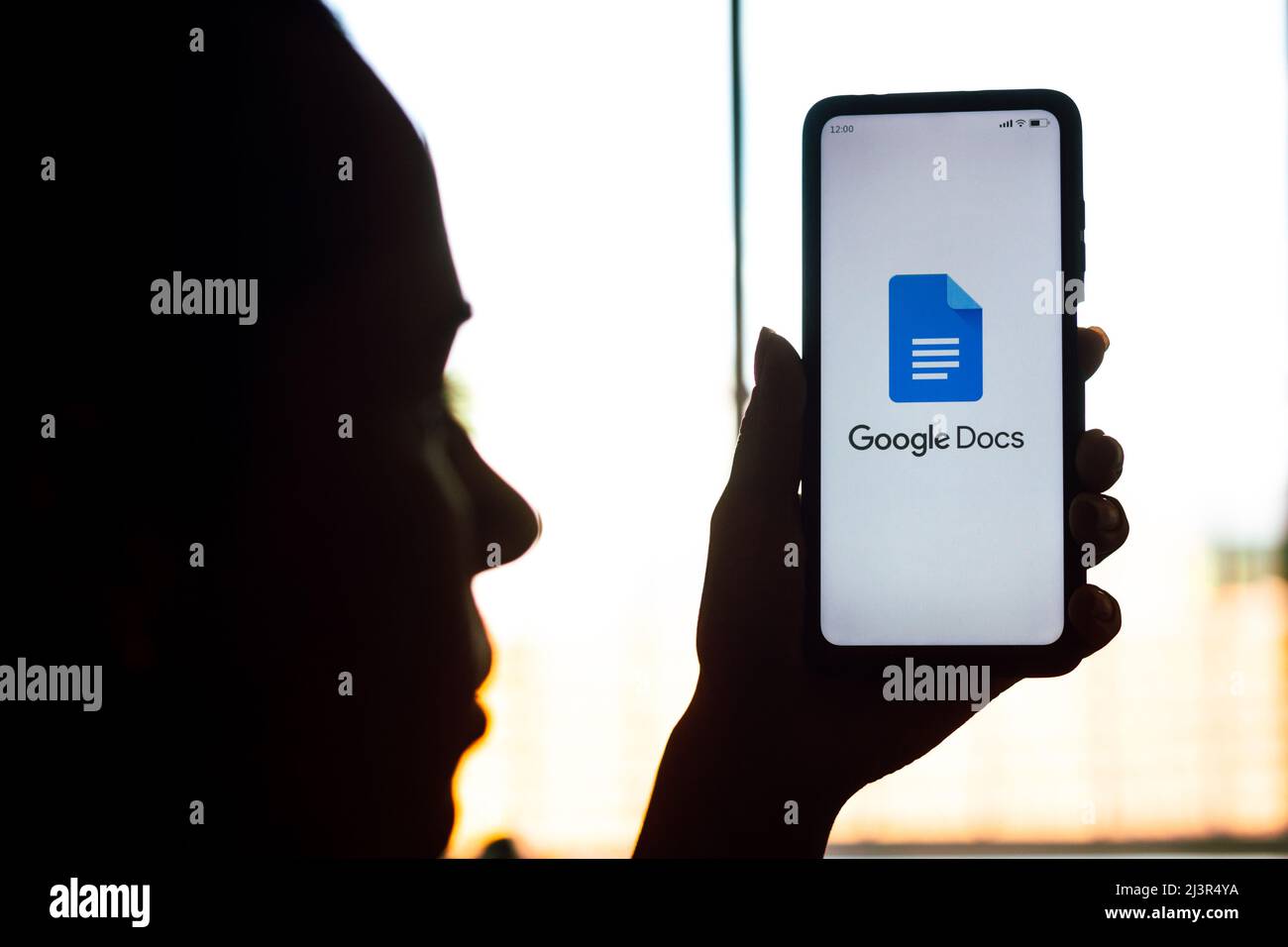 In this photo illustration, a woman's silhouette holds a smartphone with the Google Docs logo displayed on the screen. Stock Photo