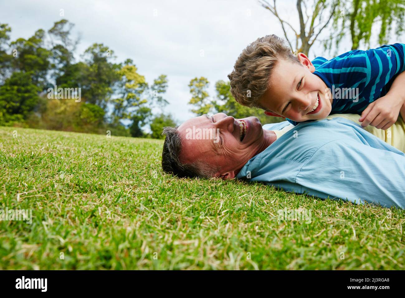 Sharing moments between father and son. Shot of a laughing father and son lying on grass. Stock Photo