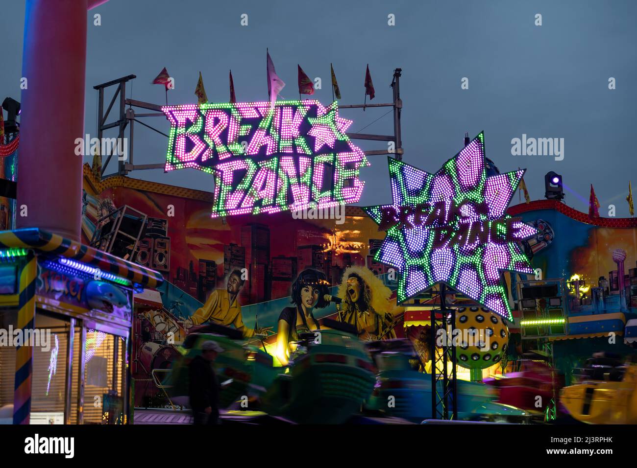 Breakdance funfair ride with a big illuminated logo in the evening. The fairground ride is spinning very fast. Leisure activities in Germany Stock Photo