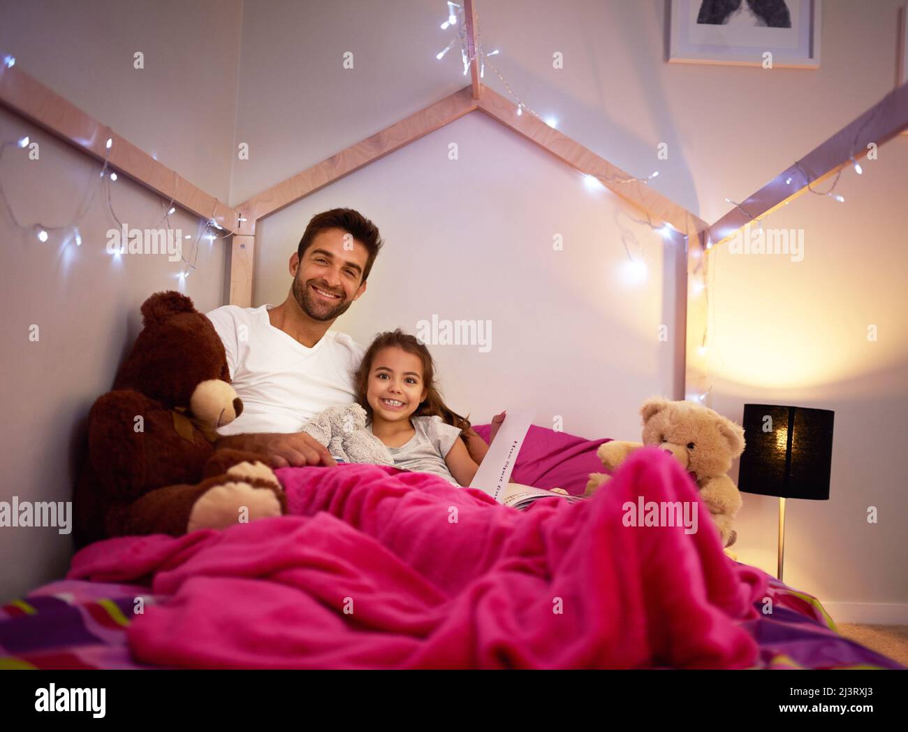 Whats a bedtime routine without a bedtime story. Portrait of a father reading a book with his little daughter in bed at home. Stock Photo