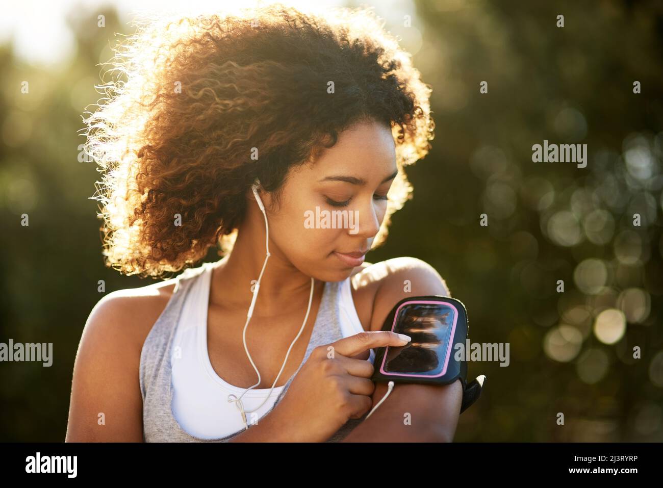 Pick the playlist that gets you going. Shot of an attractive young woman listening to music while exercising outdoors. Stock Photo