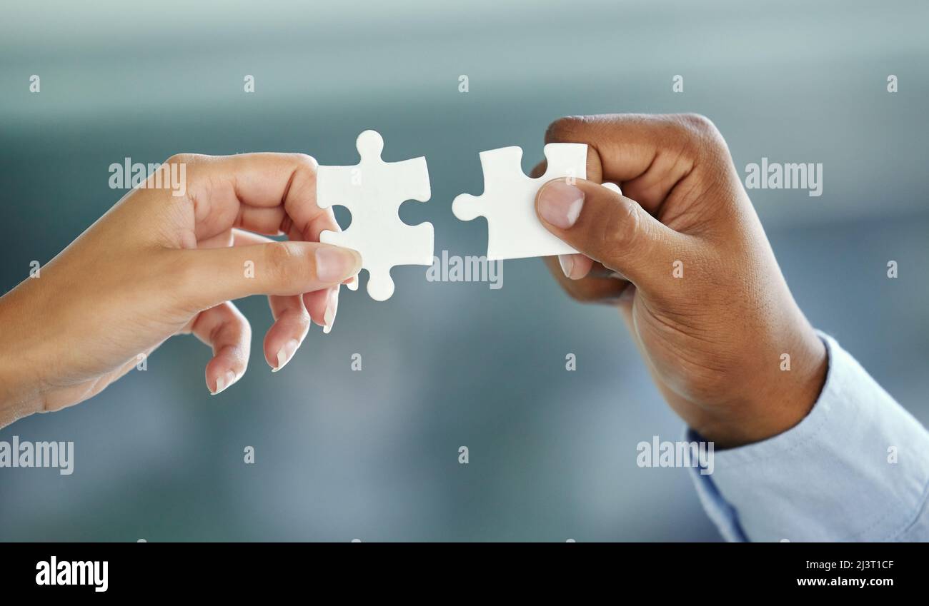 Putting the pieces together. Cropped shot of two unrecognizable businesspeople fitting puzzle pieces together while standing in their office. Stock Photo