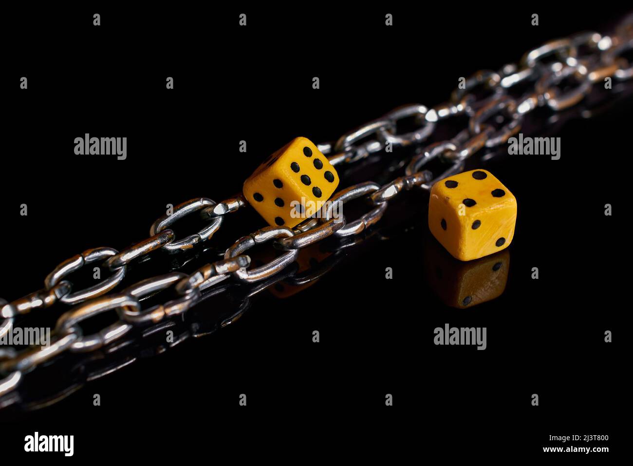 Gambling addiction. Two dice and a chain on a black background with reflection Stock Photo