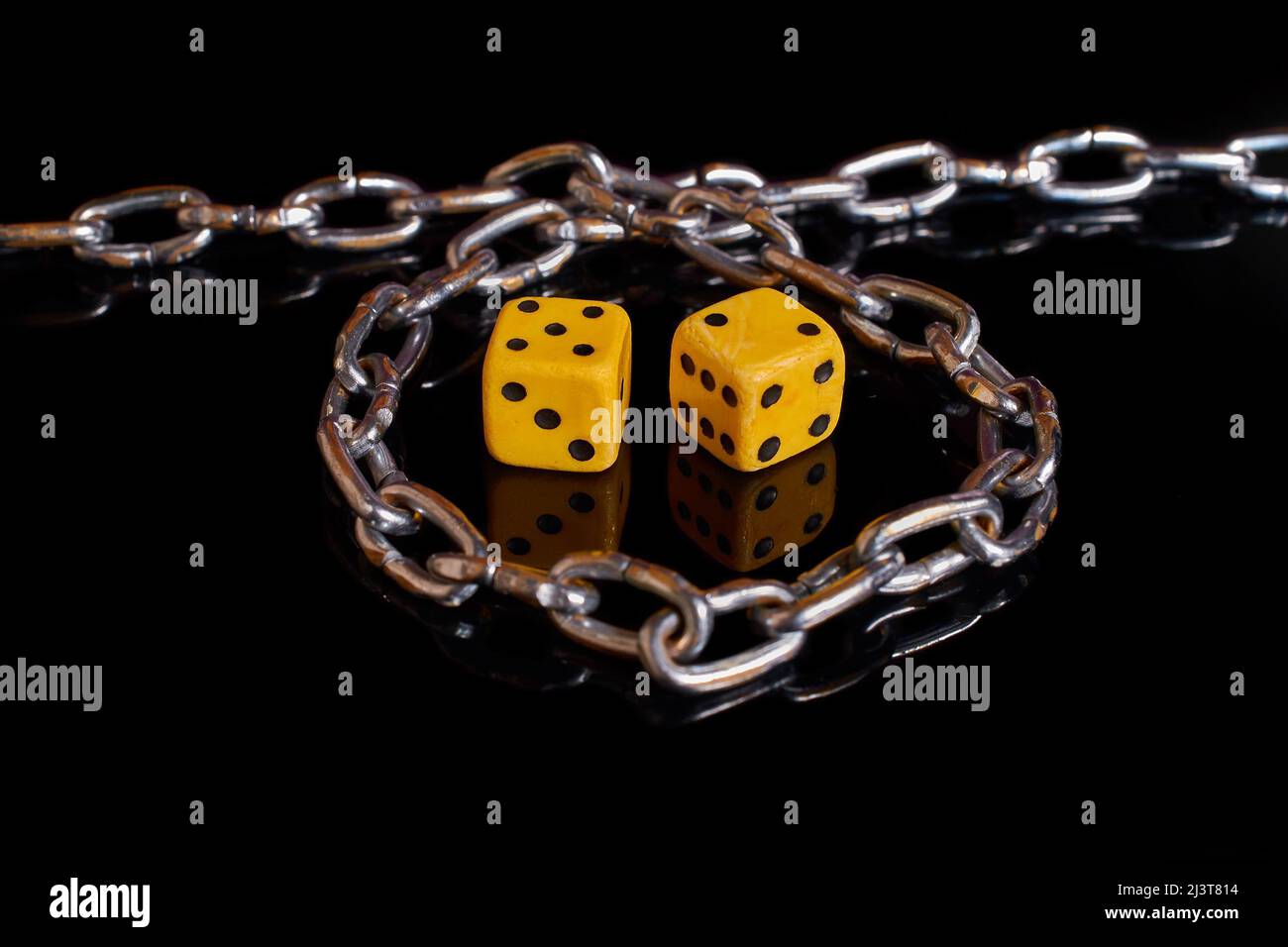Gambling addiction. Two dice wrapped in a chain on a black background  Stock Photo