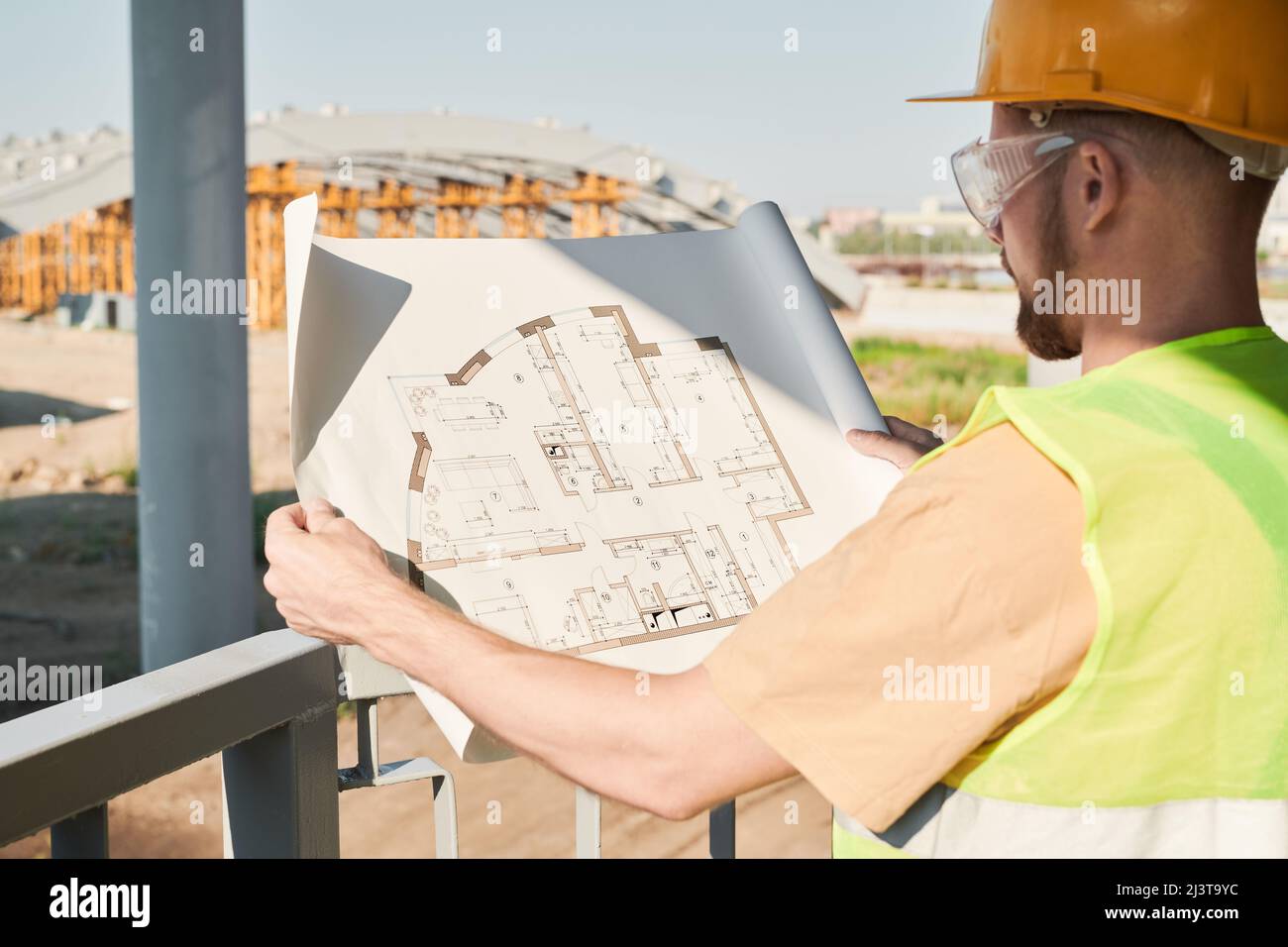Construction engineer wearing safety vest and work helmet standing at construction site and working on apartment building project Stock Photo
