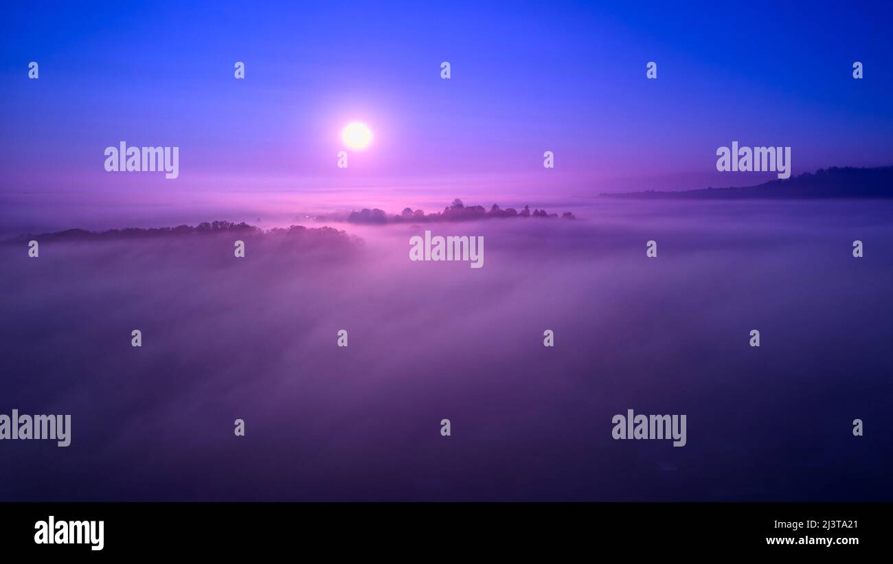 The sun rises above the fog. Small village surrounded by trees ...