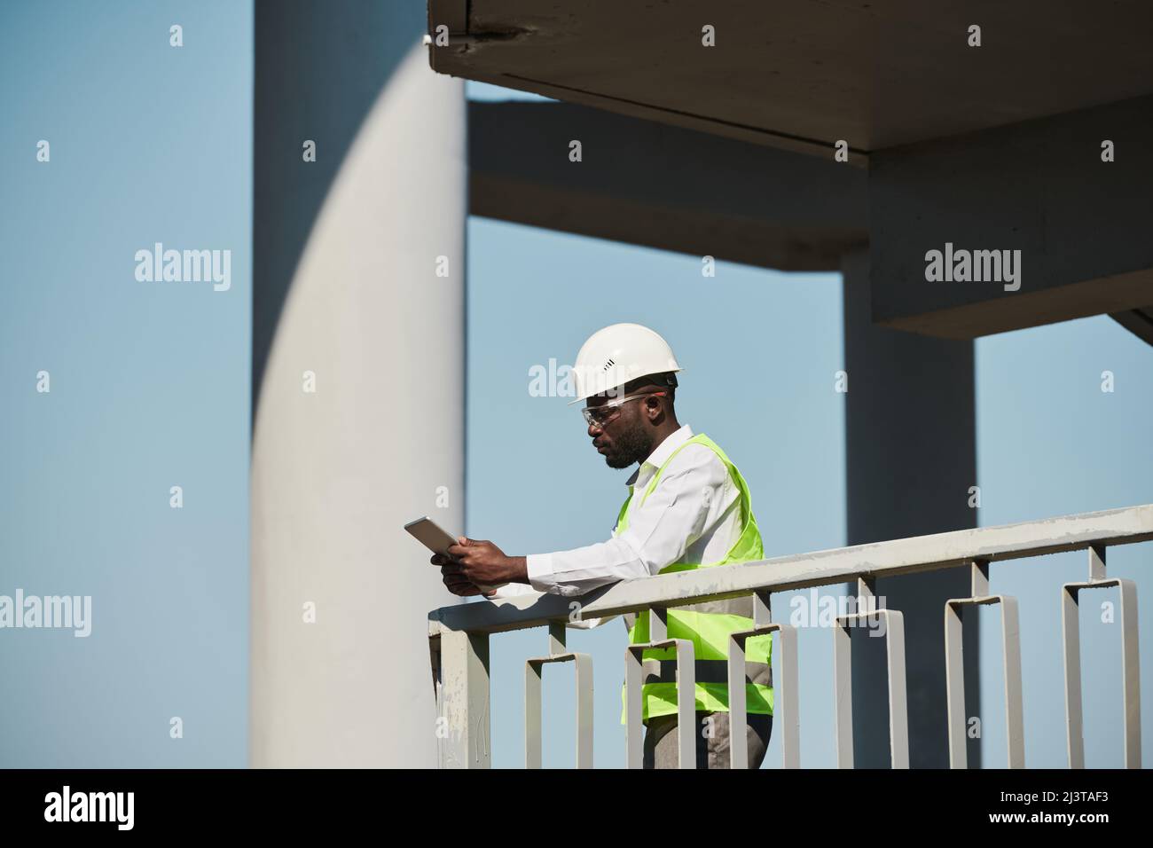 Side view portrait of young black engineer wearing hardhat on construction site against sky, copy space Stock Photo