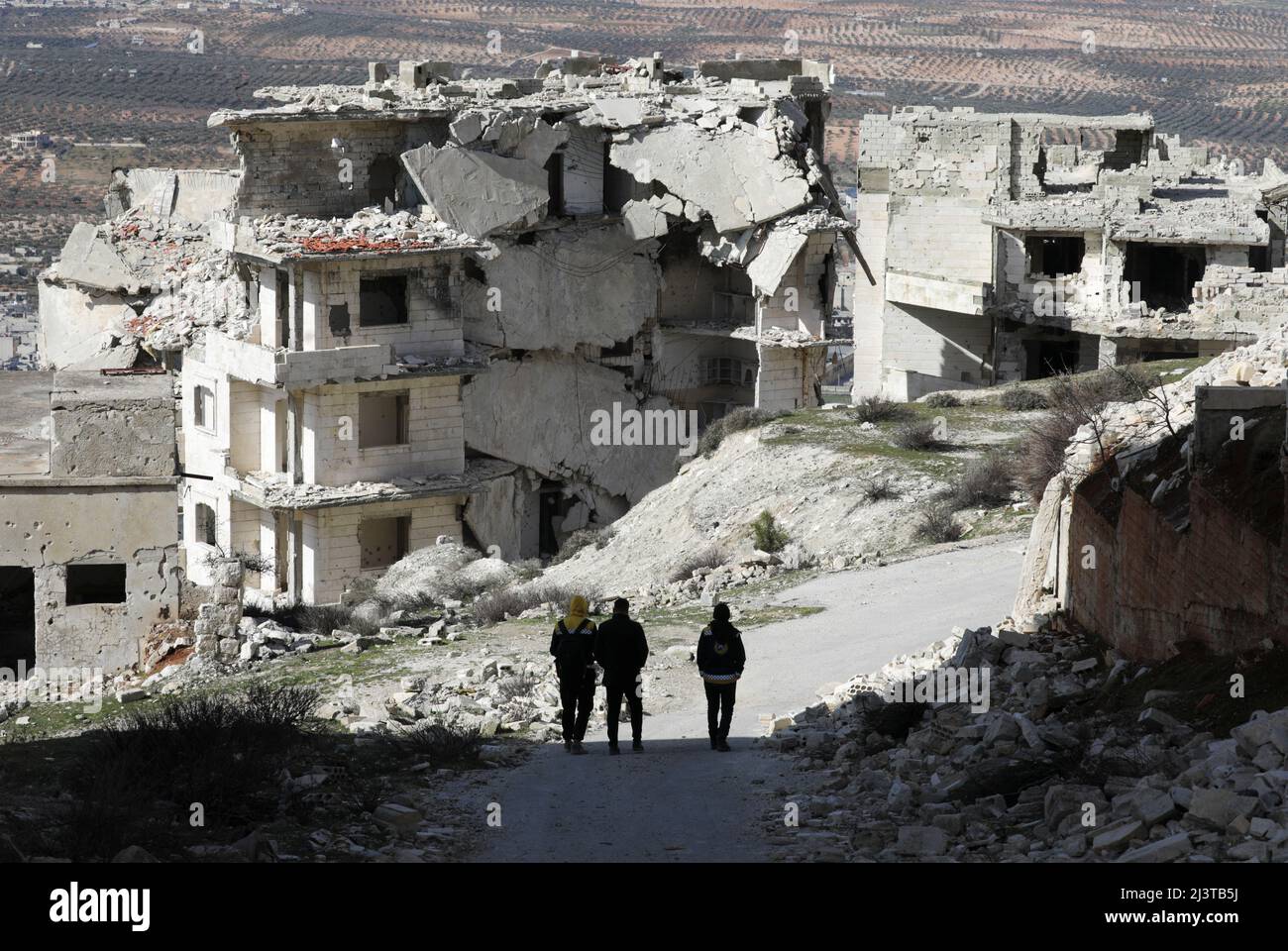 People walk past damaged buildings in the rebel-held Jabal al-Arbaeen, in the southern province of Idlib, Syria March 20, 2022. Picture taken March 20, 2022.  REUTERS/Khalil Ashawi Stock Photo