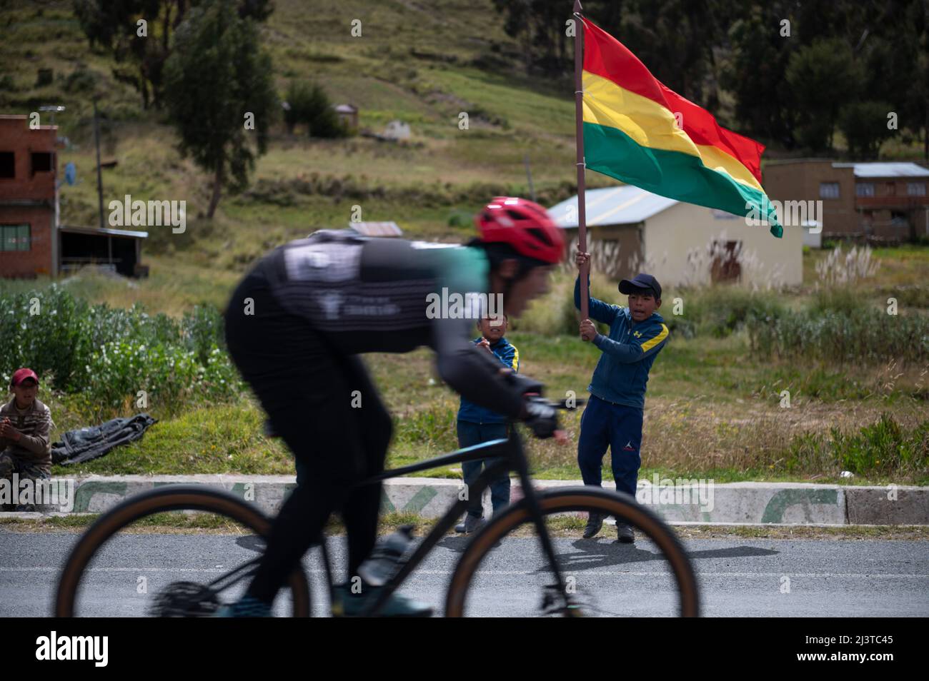 Jankho Amaya, Bolivia. 09th Apr, 2022. Children holding a Bolivian flag cheer on a cyclist during a bike race. The 'Poncho rojo' (red poncho) race, named after the typical garment worn by local authorities, attracts both professional and amateur participants and runs along the shores of Lake Titicaca at altitudes ranging from 3800 to 4000 meters above sea level. This year, more than 450 cyclists of all ages have registered for the event, which is either 52 or 97 kilometers long. Credit: Radoslaw Czajkowski/dpa/Alamy Live News Stock Photo