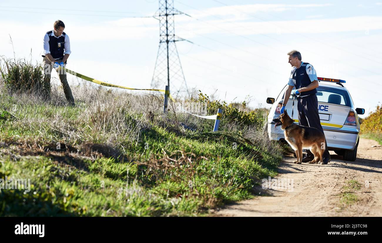 Let him get the scent. Shot of two policemen cordoning off a crime scene with police tape. Stock Photo