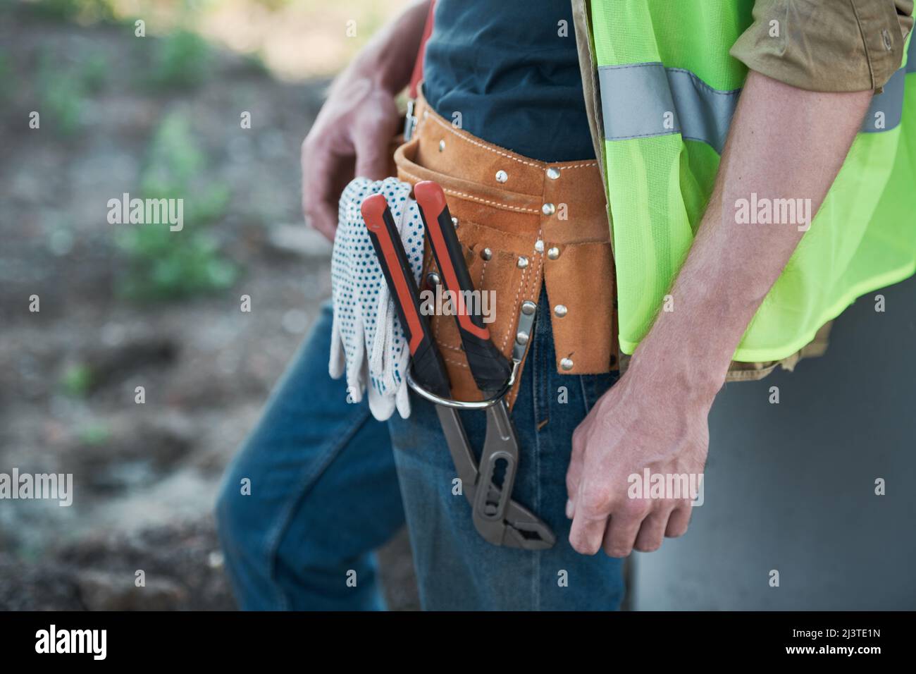 Unrecognizable workman wearing green vest and holding toolbox on construction site Stock Photo