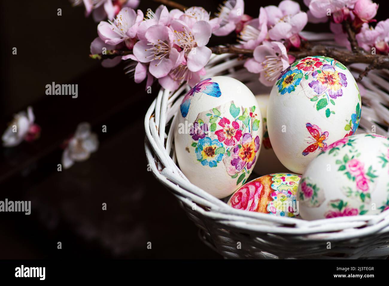 White Easter eggs made with decoupage technique with floral motifs and a flowering branch on a black rustic background. Stock Photo