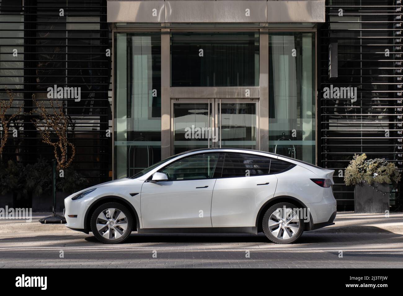 A white Tesla Model Y is seen parked at the front of a building in downtown Toronto. Stock Photo
