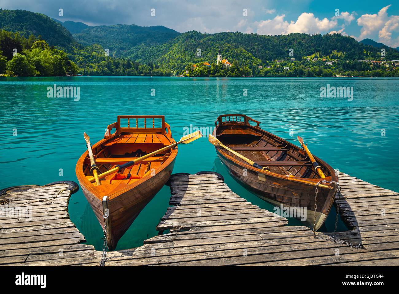 Wooden rowing boats moored at the pier. Rowing boats on the lake Bled and Pilgrimage church with small island in background, Slovenia, Europe Stock Photo
