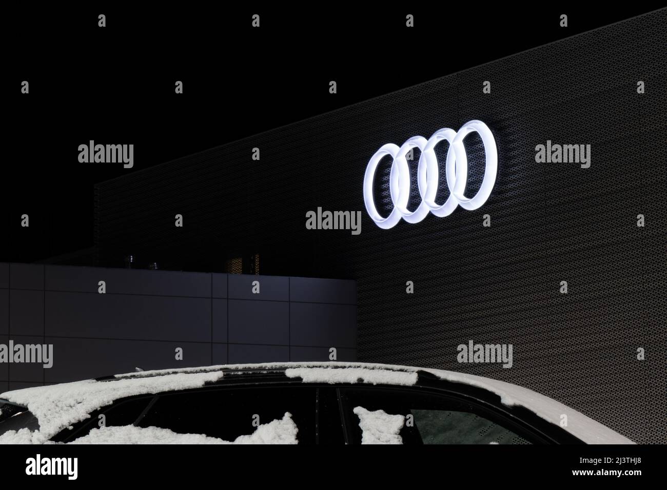 The famous four-ring Audi logo is illuminated at night on the side of an Audi car dealership. Stock Photo