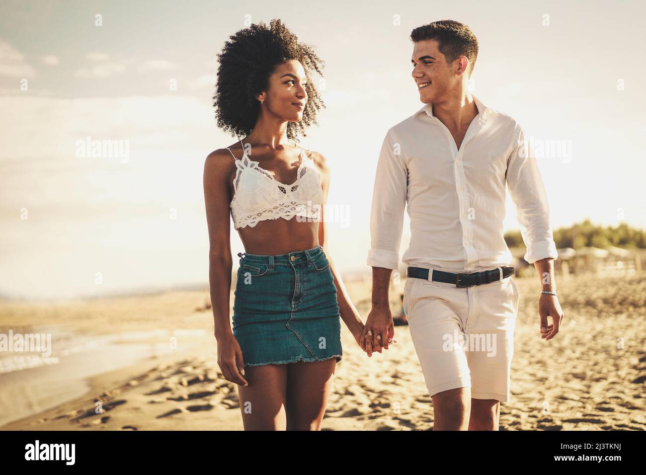 Gen z biracial couple of newlyweds on vacation on the beach walking