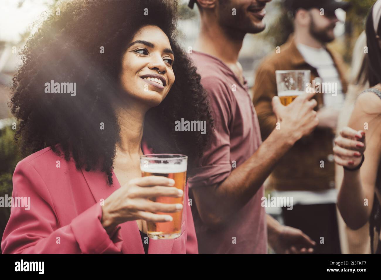 cheerful trendy Brazilian girl in a students rooftop party holding a glass of beer - social event with people gathering to hostel patio party the end Stock Photo