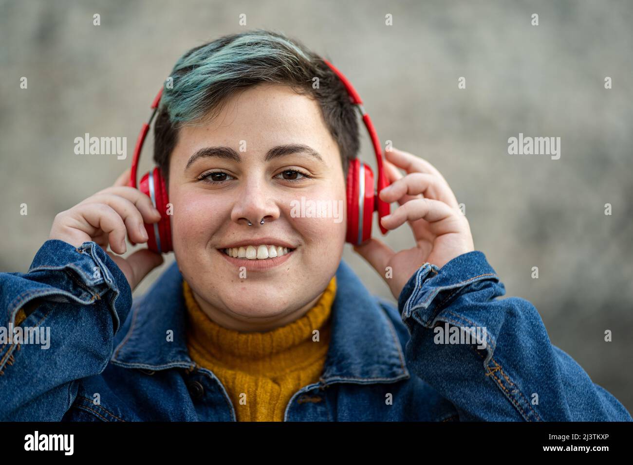 Portrait of an androgynous looking girl dressed in jeans with short, colorful hair, wears a red wireless headset Stock Photo