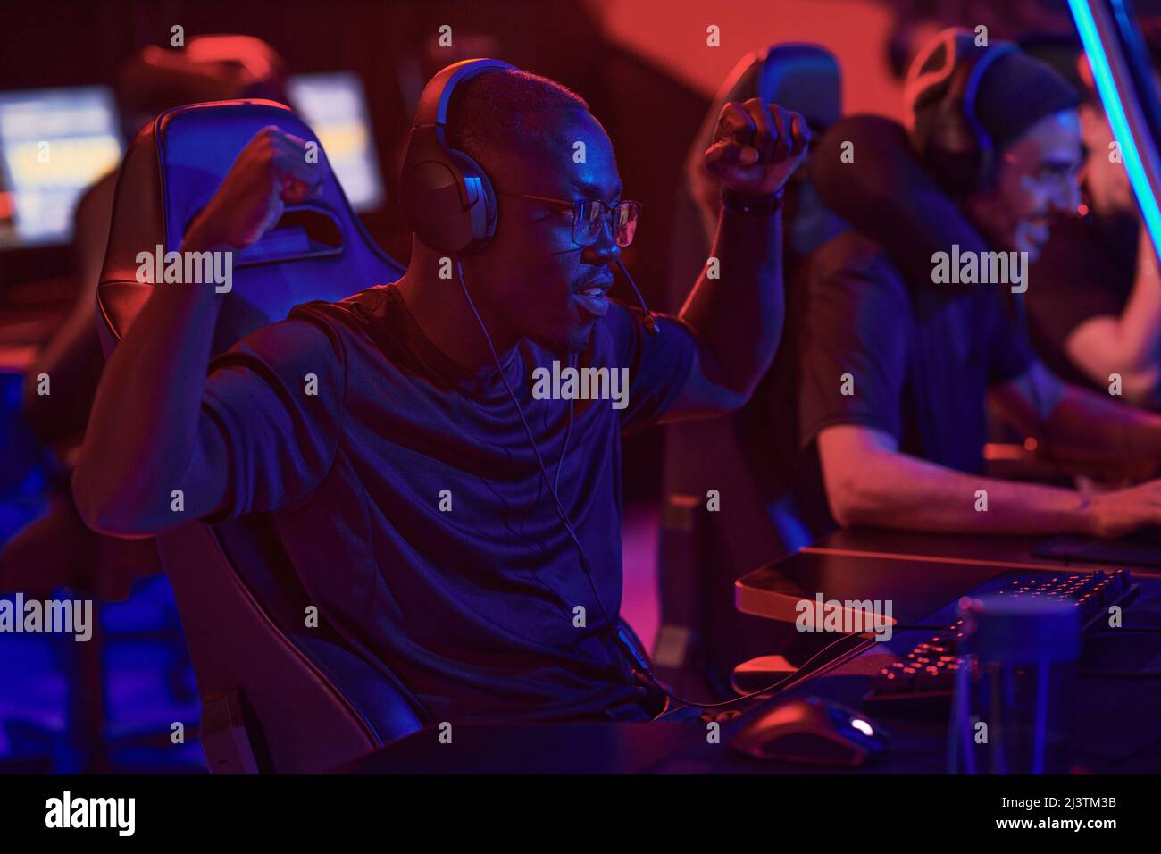 Positive young Black guy in headphones gesturing hands like monkey while winning game, he participating in esports championship Stock Photo