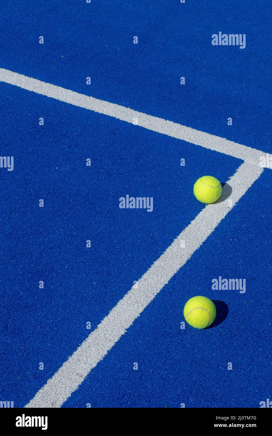 two balls next to the lines of a blue paddle tennis court, racket