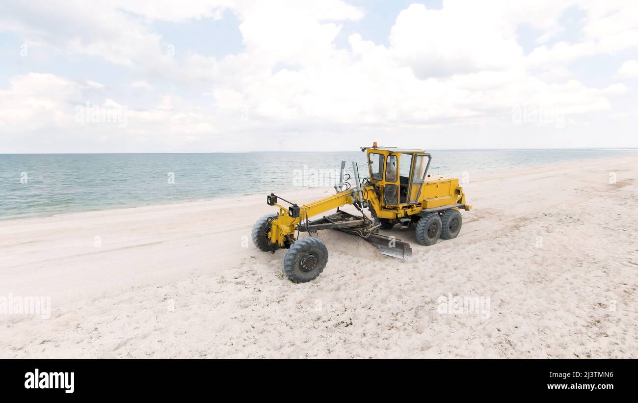Top view of tractor on beach. Action. Bulldozer clears white beach by ...