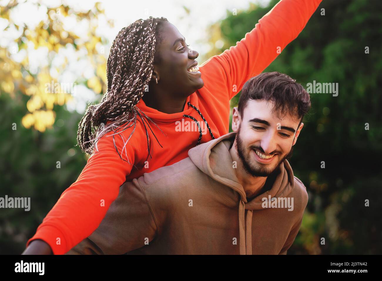 Portrait of overjoyed gen z biracial woman piggyback hug smiling caucasian boyfriend man Stock Photo