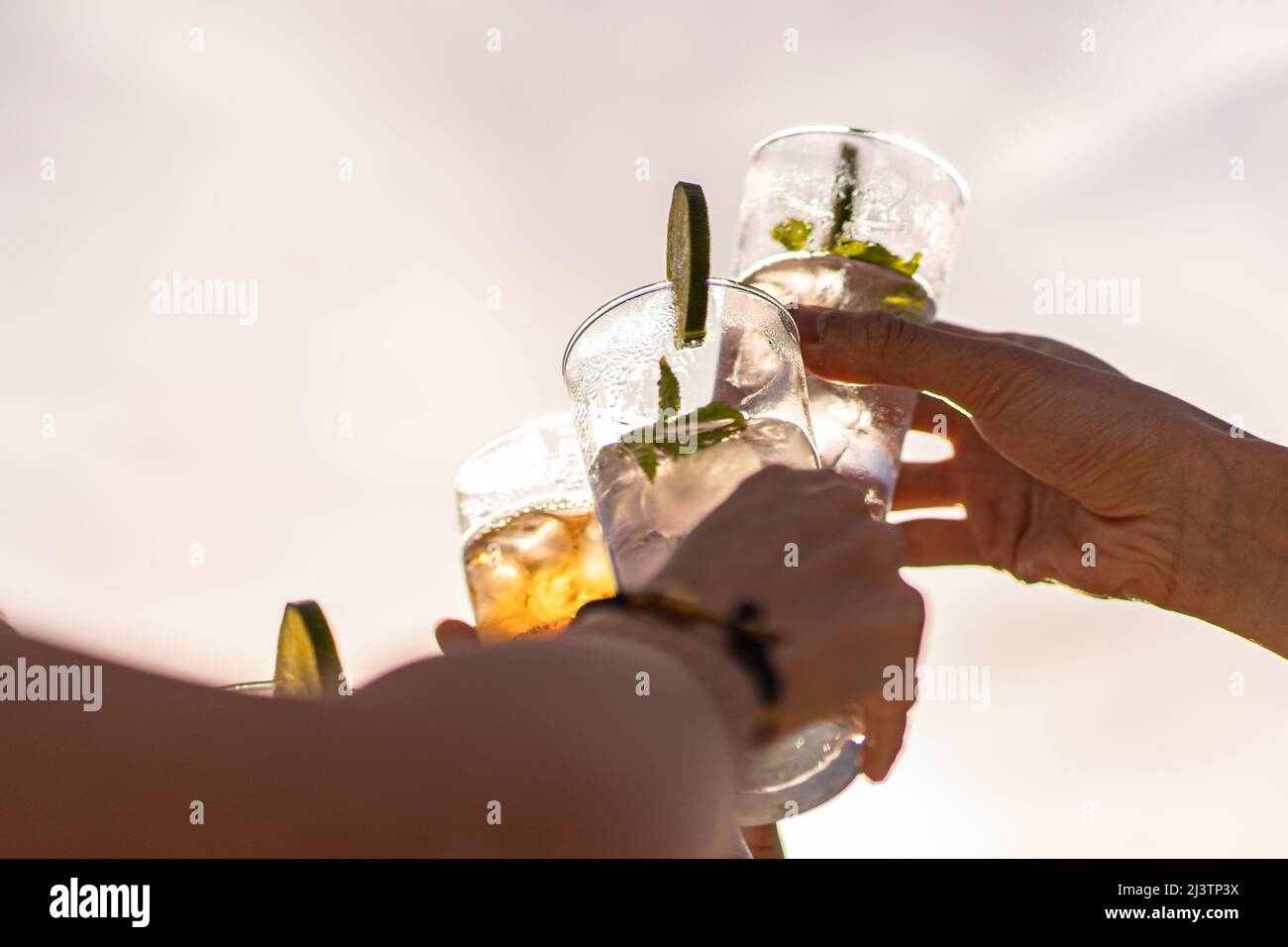 Friends rising cocktail glasses for a celebratory toast against the sky in the summer Stock Photo