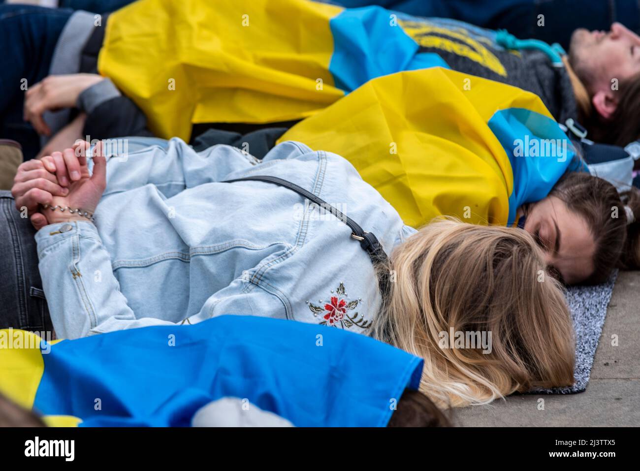 Protesters carrying out a die-in, referencing the killed Ukraine civilians in towns such as Bucha during war with Russia. Females play dead with flag Stock Photo