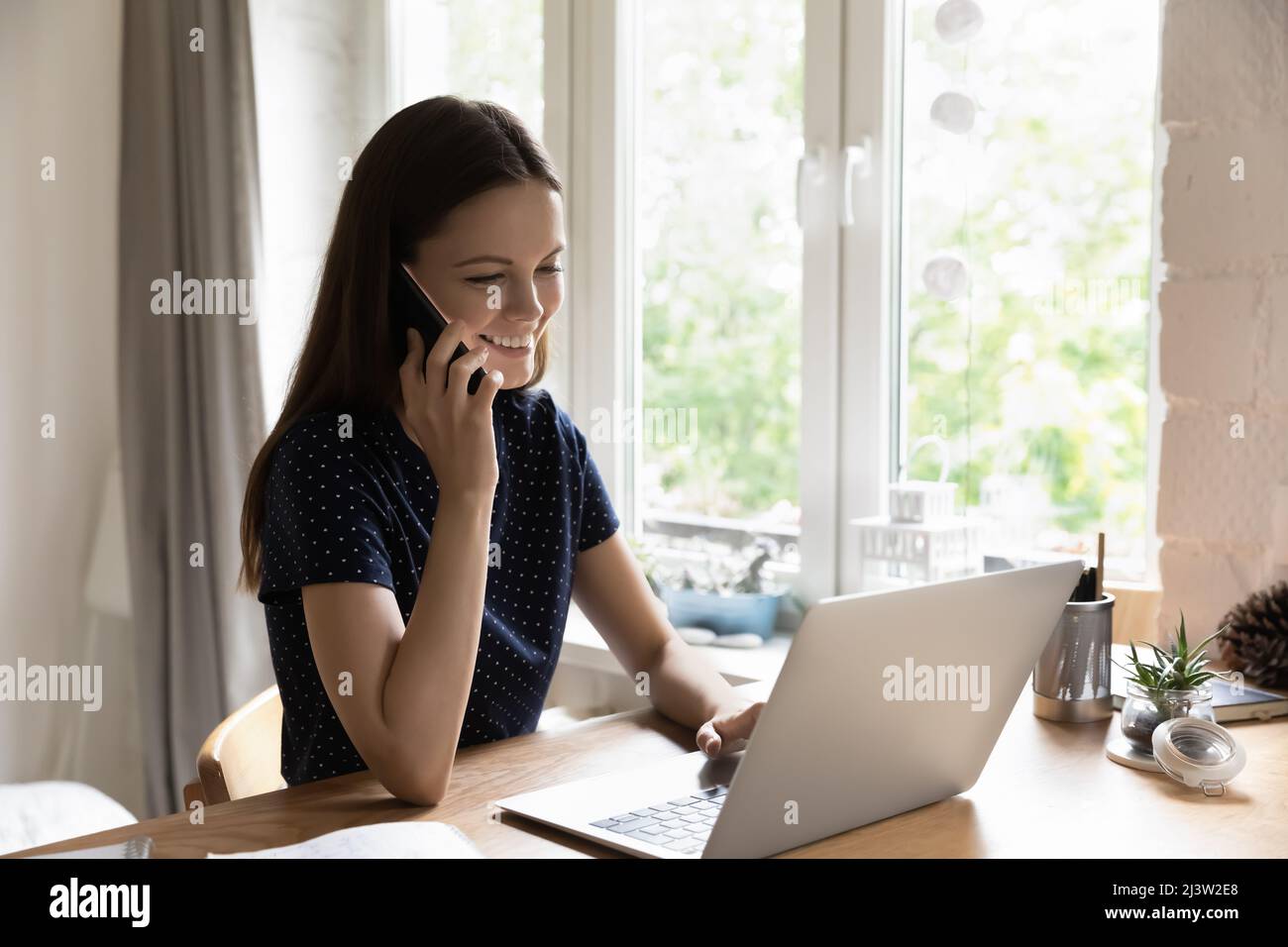 Woman sit at table with laptop enjoy conversation on cellphone Stock Photo