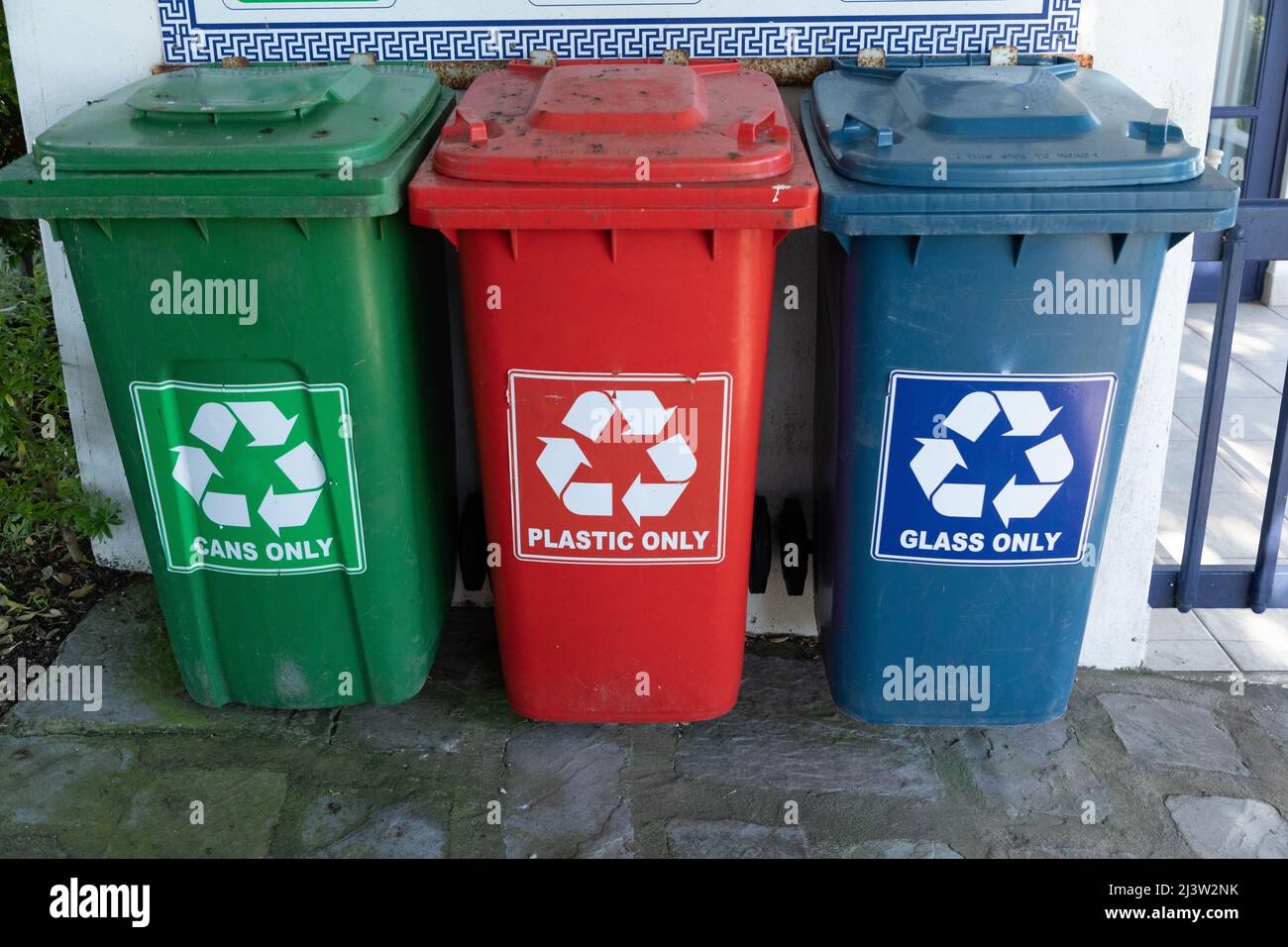 Three different coloured plastic bins for recycling. Green for cans red for plastic and a blue bin for glass. Stock Photo
