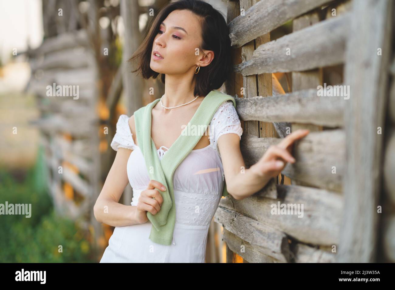 Asian woman, posing near a tobacco drying shed, wearing a white dress and green wellies. Stock Photo