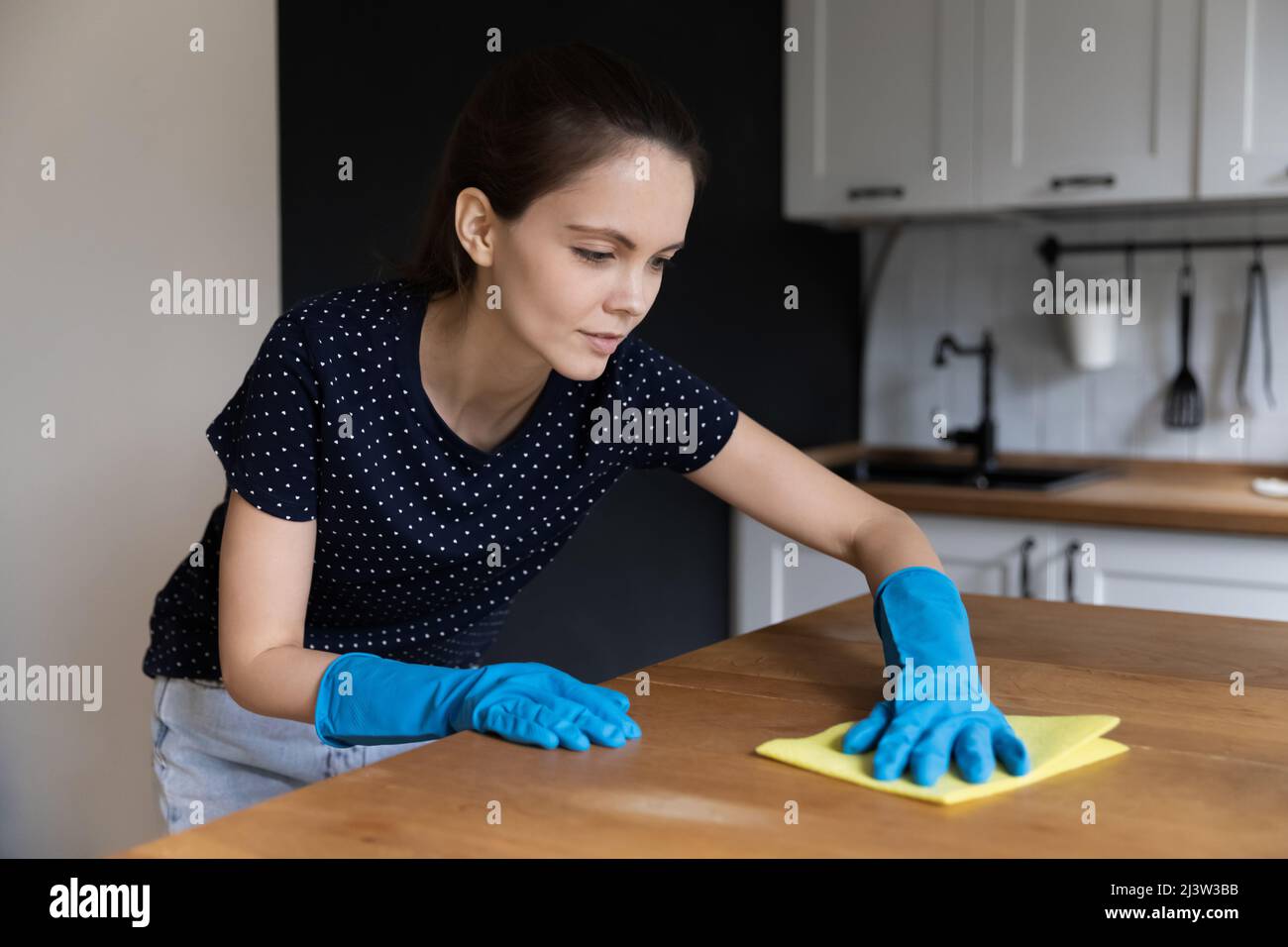 Young woman wear rubber gloves cleans kitchen table Stock Photo