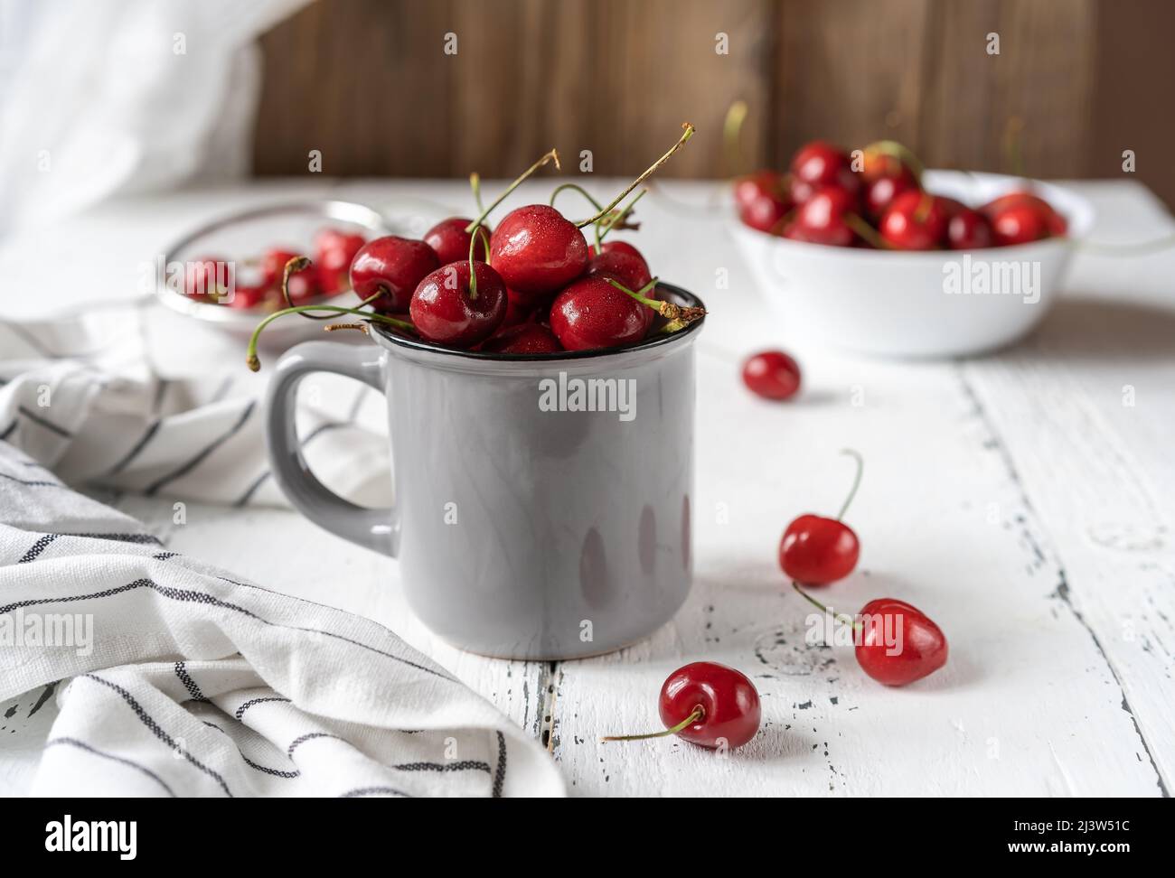 Fresh sweet cherries on plate and jar on white wooden table with blue flowers Stock Photo