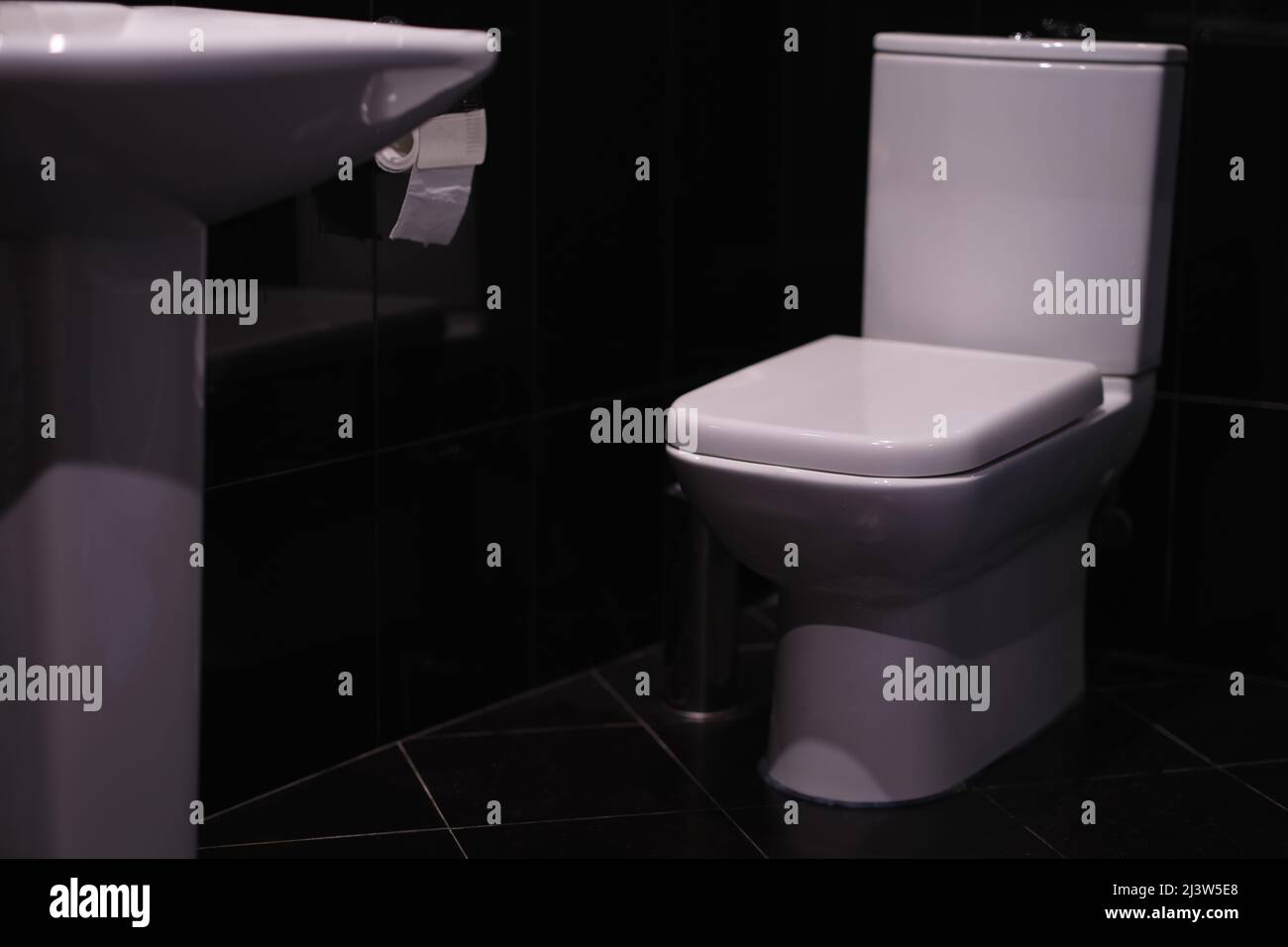 White toilet standing in bathroom with black tiles Stock Photo - Alamy