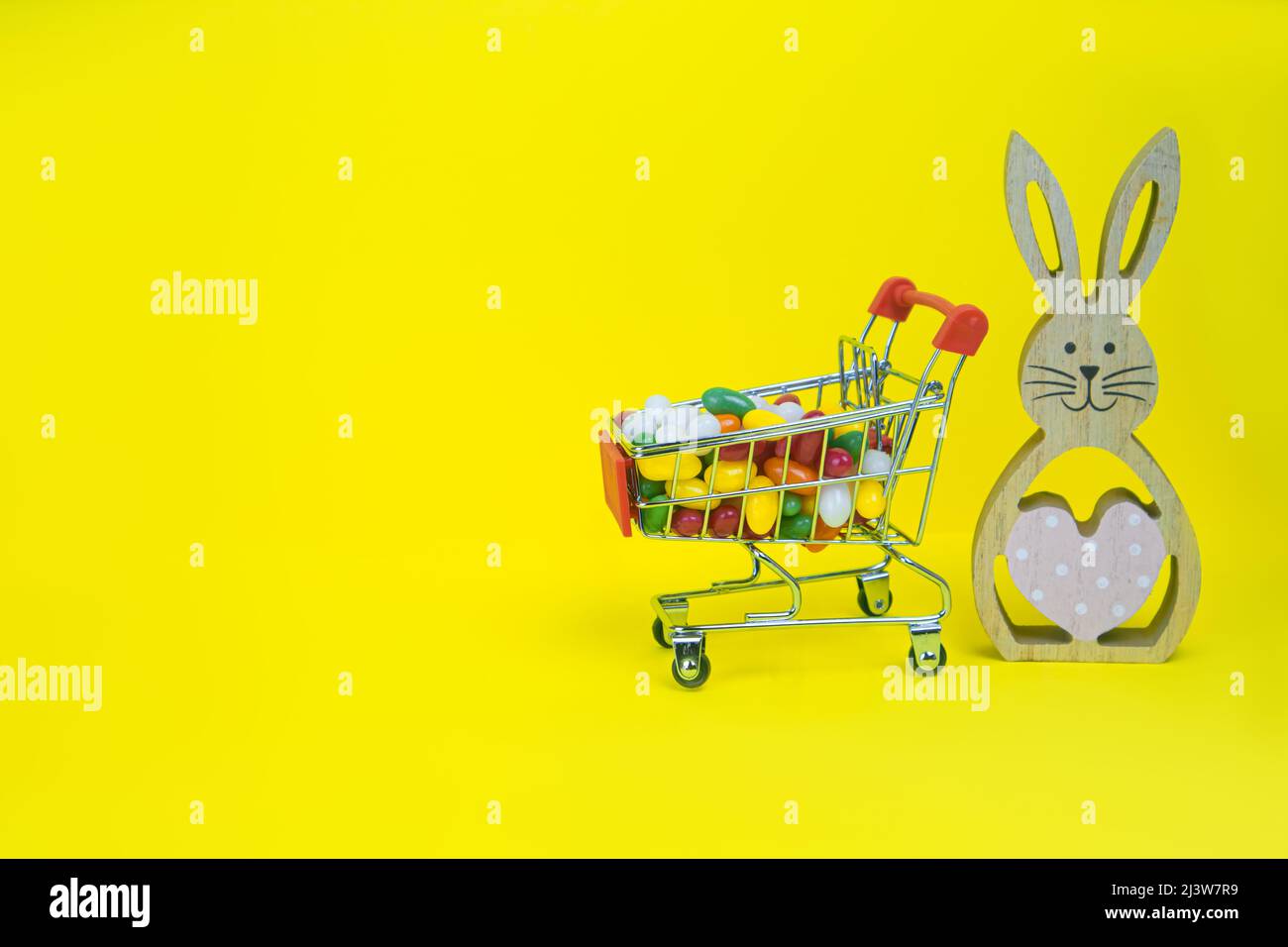 https://c8.alamy.com/comp/2J3W7R9/wooden-easter-bunny-and-shopping-cart-with-candies-on-yellow-background-2J3W7R9.jpg