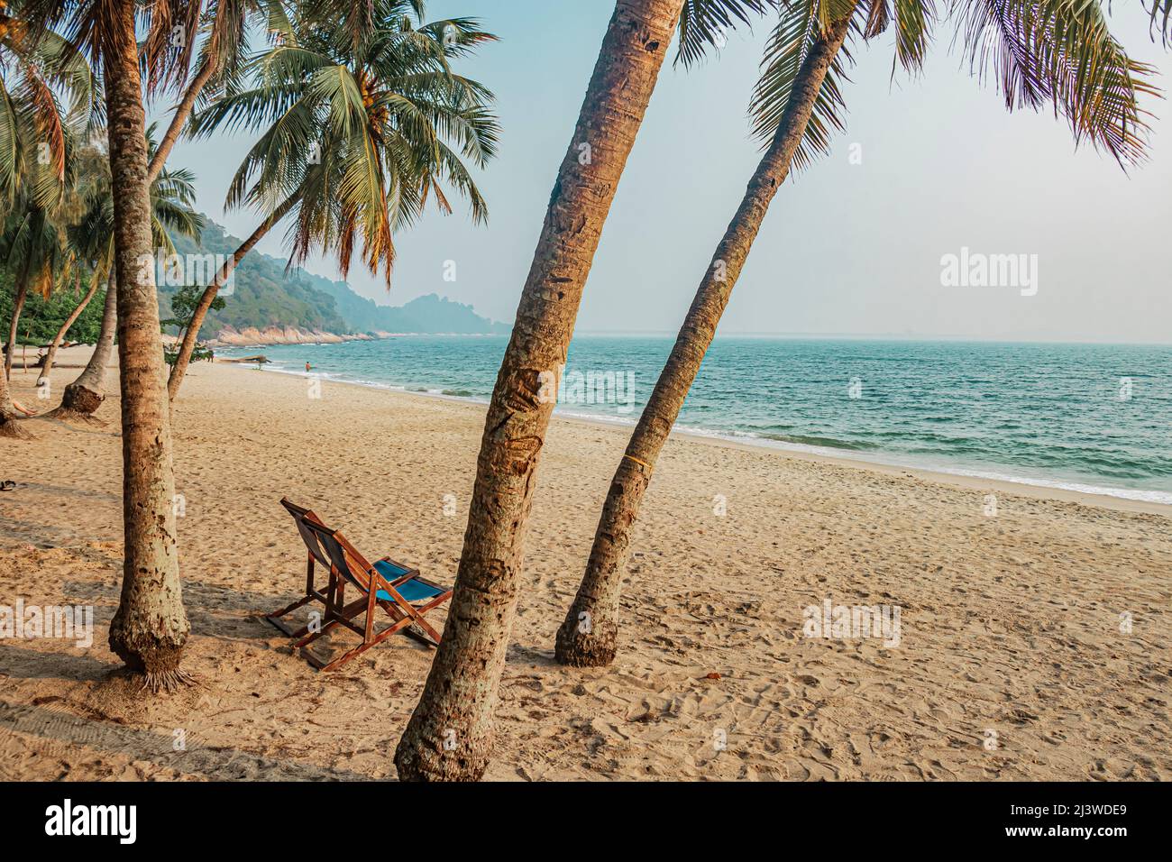 An empty chair on sandy beach between the coconut trees at Teluk Batik Beach near Lumut in Perak, Malaysia. Stock Photo