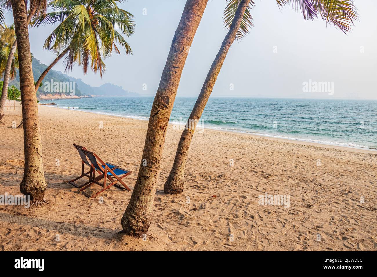 An empty chair on sandy beach between the coconut trees at Teluk Batik Beach near Lumut in Perak, Malaysia. Stock Photo