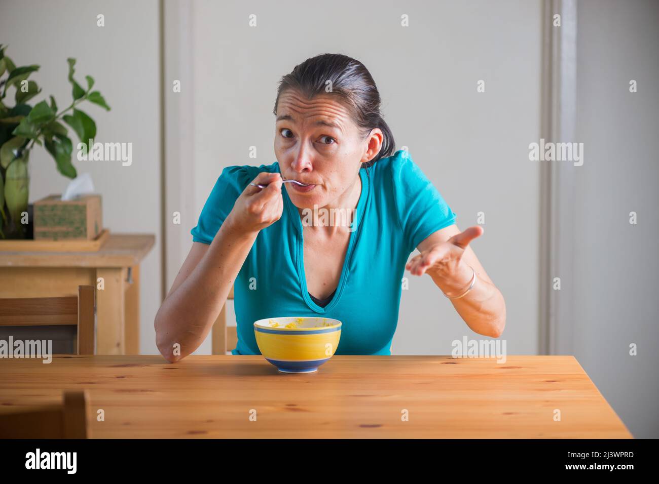 Woman eating kitchari for a breakfast and making funny faces. Indian cuisine. Lifestyle portrait. Stock Photo