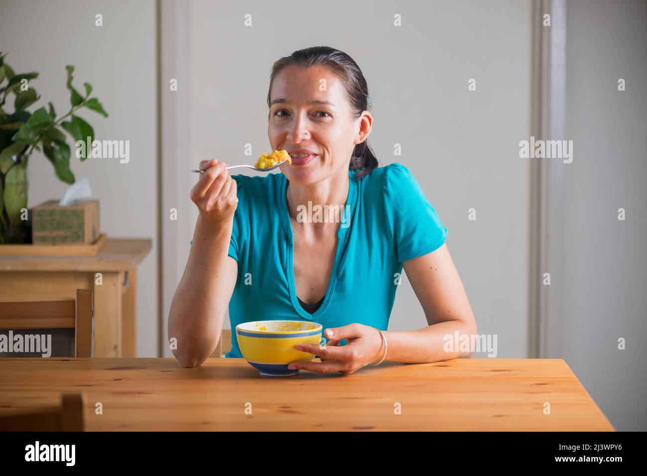 Smiling woman eating kitchari for a breakfast. Indian cuisine. Lifestyle portrait. Stock Photo