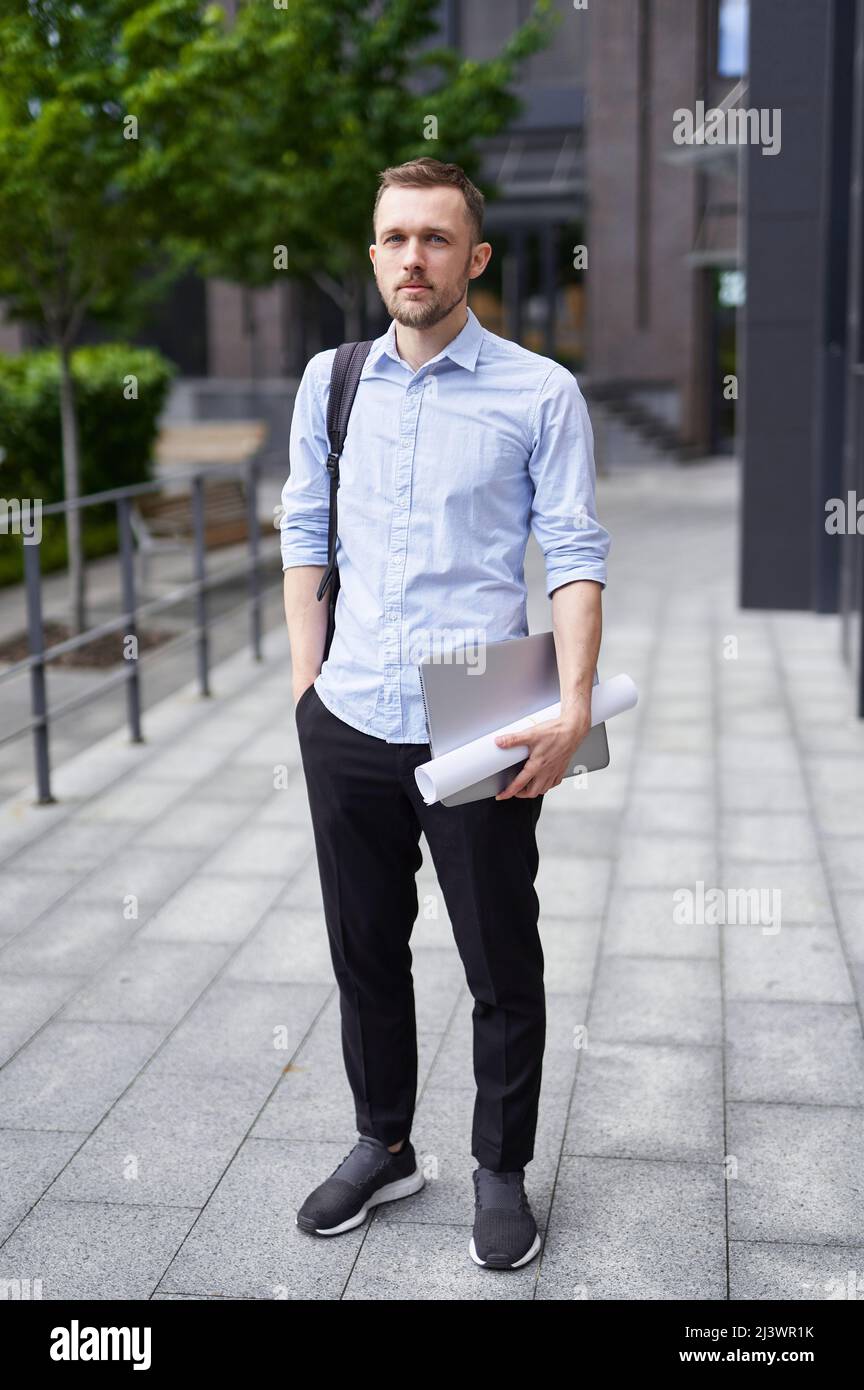 Successful and confident businessman outdoor. Urban background of a modern office building in downtown. Young smiling stylish bearded business man standing on a street. High quality image Stock Photo
