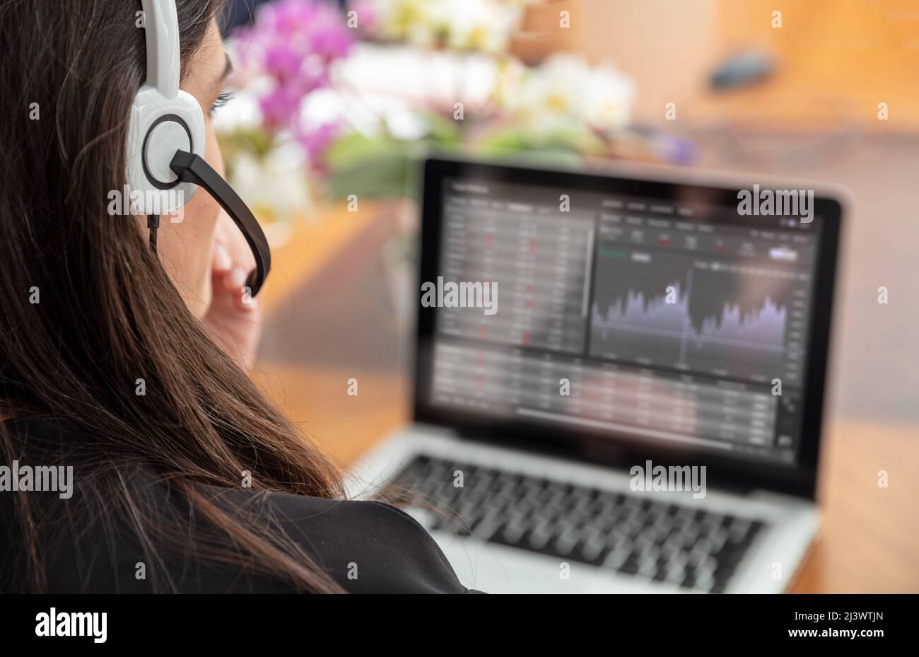 Home office, customer support, help desk concept. Woman with headset working with a laptop, talking on phone, view from behind. Stock Photo