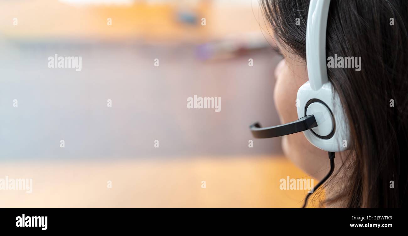 Call center, home office, customer support, help desk concept. Woman with headset talking on phone, close up view from behind. Copy space Stock Photo