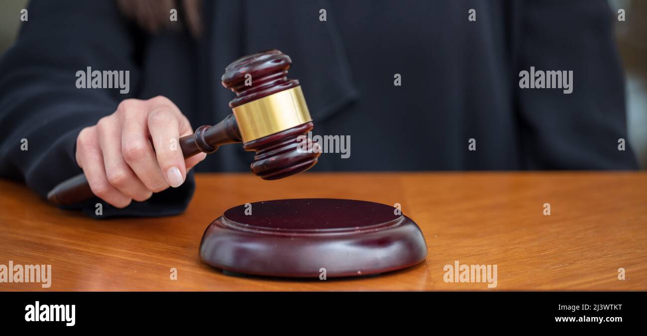 Judge female hand holding a gavel on wooden law court bench, close up above view. Justice and punishment concept Stock Photo
