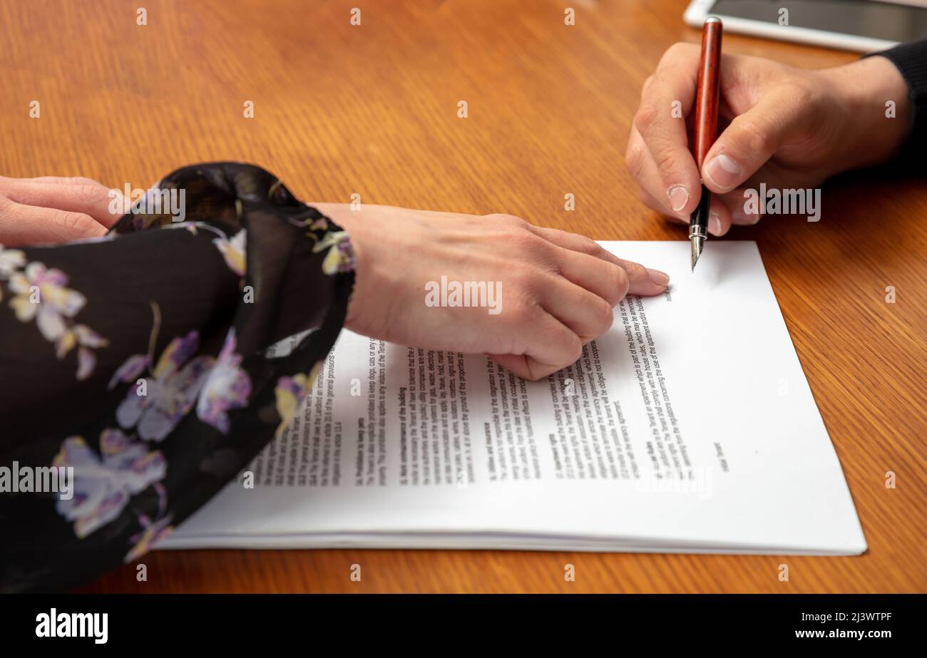 Woman and man hands and legal papers for signature on a wooden table, lawyer office. Agreement signing, business contract documents. Stock Photo