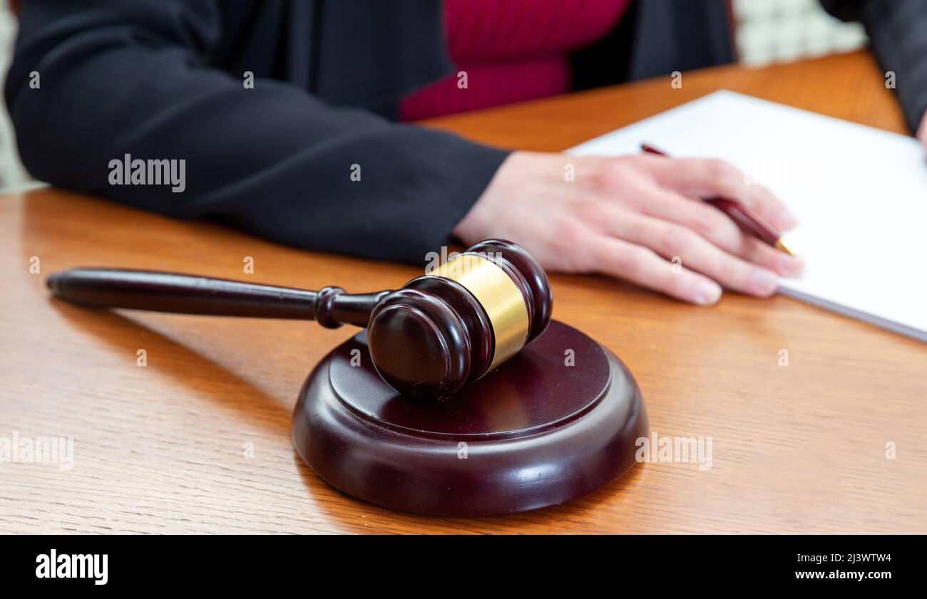 Auction judge gavel on a wooden table close up view. Woman sitting with crossed hands and a notepad infront her Stock Photo